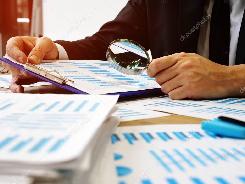 The auditor makes audit and verifies the report using a magnifying glass.