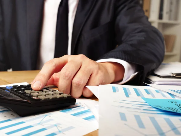 Человек рассчитывает годовой финансовый отчет с помощью калькулятора и стопки бумаги . — стоковое фото