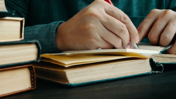 Een man leest een boek en maakt aantekeningen in een notitieboekje. Een close-up van een leerboek. — Stockvideo