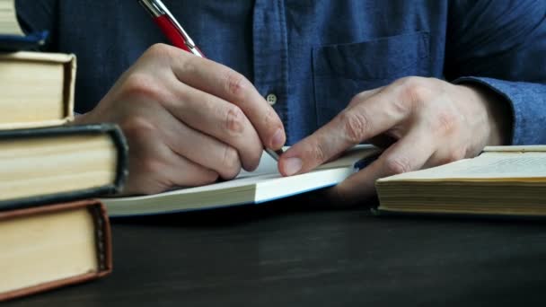 Zbliżenie rąk robiących notatki w notatniku. Człowiek studiuje i czyta książkę w bibliotece.. — Wideo stockowe