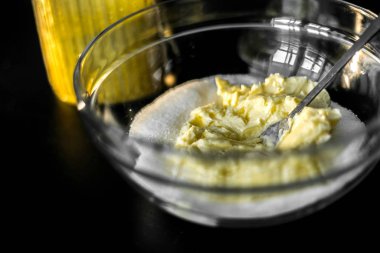 Yumuşak tereyağlı ve şekerli bardakta, çatalla karıştırılmış. Kurabiye, pasta ve kek için hamur hazırlığı. Siyah bir masa ve bir kavanoz şeker..