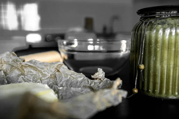 Ingredientes e utensílios para fazer biscoitos e cozinhar no fundo da cozinha. Manteiga amarela, papel manteiga e açúcar em uma tigela de vidro em uma mesa preta . — Fotografia de Stock