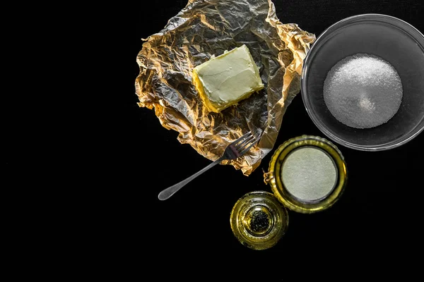 Kurabiye ve yemek yapmak için gerekli malzemeler. Sarı tereyağı, siyah masadaki cam tabakta şeker. Yukarıdan görünüşü