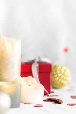New year and Christmas card, colorful red and gold baubles with a gift box, candles and confetti on a white blurred background. selective focus. space for text