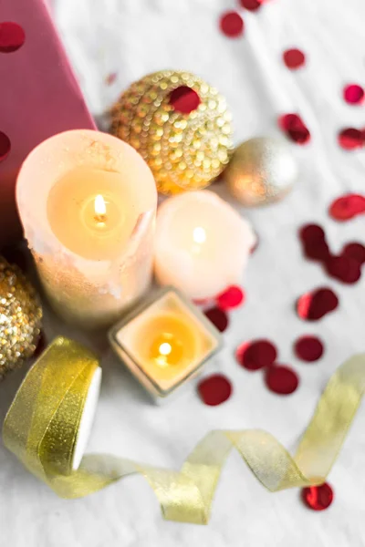 New year and Christmas card, colorful gold and silver baubles with a gift box, ribbon, candles and confetti on a white background. selective focus. top view