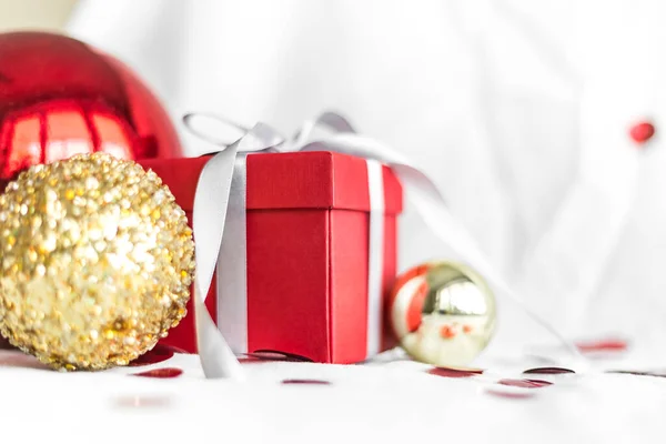 New year and Christmas card, colorful red and gold baubles with a gift box and confetti on a white blurred background. selective focus. space for text