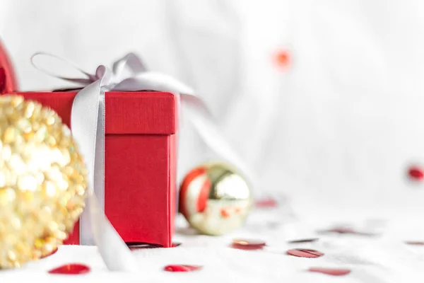 New year and Christmas card, colorful red and gold baubles with a gift box and confetti on a white blurred background. selective focus. space for text