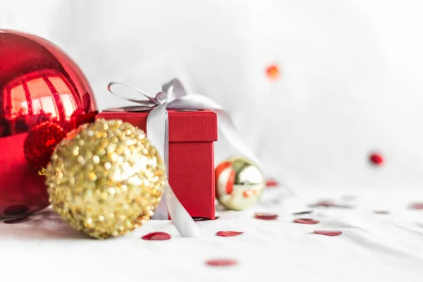 New year and Christmas card, colorful red and gold baubles with a gift box and confetti on a white blurred background. selective focus. space for text
