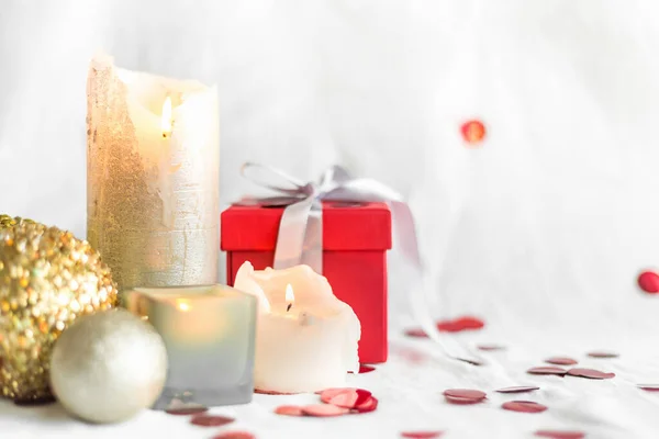 New year and Christmas card, colorful red and gold baubles with a gift box , candles and confetti on a white blurred background. selective focus. space for text