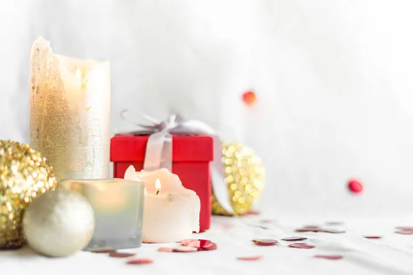 New year and Christmas card, colorful red and gold baubles with a gift box , candles and confetti on a white blurred background. selective focus. space for text