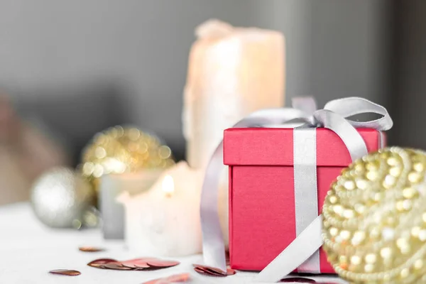 New year and Christmas card, colorful red and gold baubles with a gift box and confetti on a white blurred background. focus on the gift.