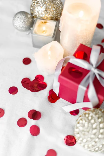 Nieuwjaars- en kerstkaart, kleurrijke rode en zilveren kerstballen met een geschenkdoos, kaarsen en confetti op een witte achtergrond. selectieve focus. bovenaanzicht — Stockfoto