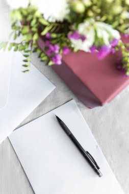 Mektup, zarf ve beyaz arka planda çiçekler olan bir hediye. Düğün davetiyesi ya da aşk mektubu. Aşk konsepti, Anneler Günün ve Sevgililer Günün kutlu olsun. Yukarıdan görünüm. Boşluğu kopyala