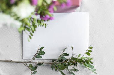 Mektup, zarf ve beyaz arka planda çiçekler olan bir hediye. Düğün davetiyesi ya da aşk mektubu. Aşk konsepti, Anneler Günün ve Sevgililer Günün kutlu olsun. Yukarıdan görünüm. Boşluğu kopyala