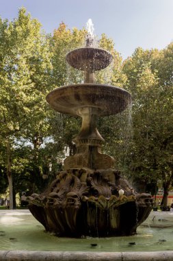 Ağaçlarla çevrili bir meydanda antik bir çeşme