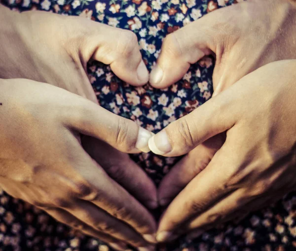 Hamile kadın ve erkek elleri kalp şeklinde.