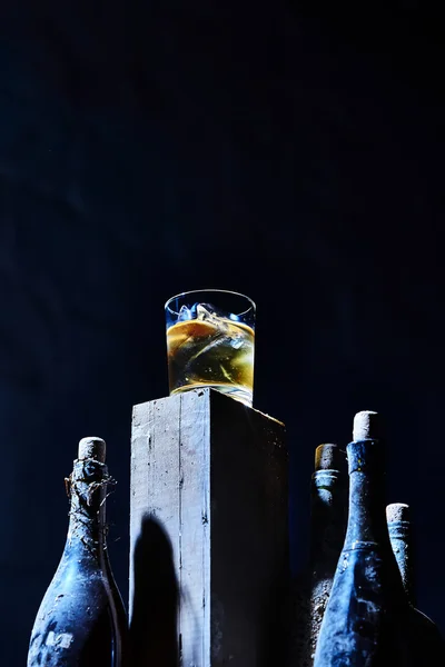 Glass of whiskey with ice on old wooden bar around the  bottles — Stock Photo, Image