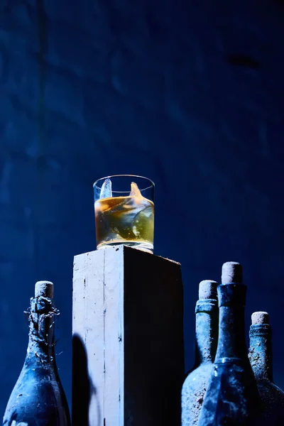 Vaso de whisky con hielo en una vieja barra de madera alrededor de las botellas — Foto de Stock