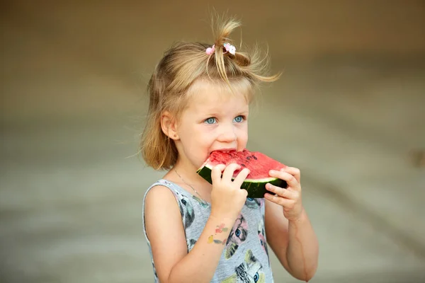 Adorable blonde girl eats a slice of watermelon outdoors. — Stock Photo, Image