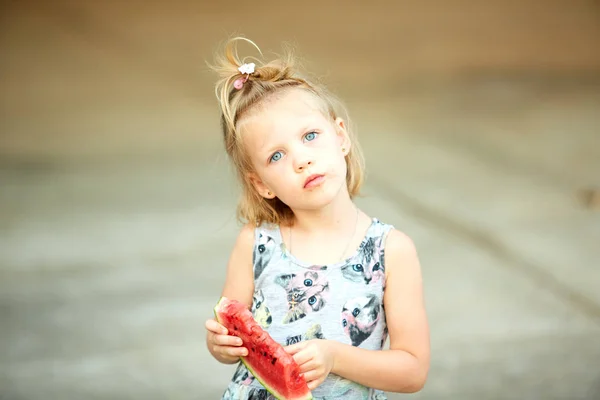 Adorable blonde girl eats a slice of watermelon outdoors. — Stock Photo, Image