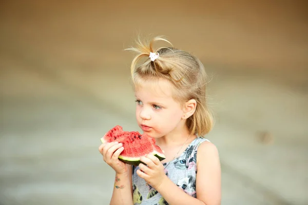 Adorable blonde girl eats a slice of watermelon outdoors. — Stock Photo, Image