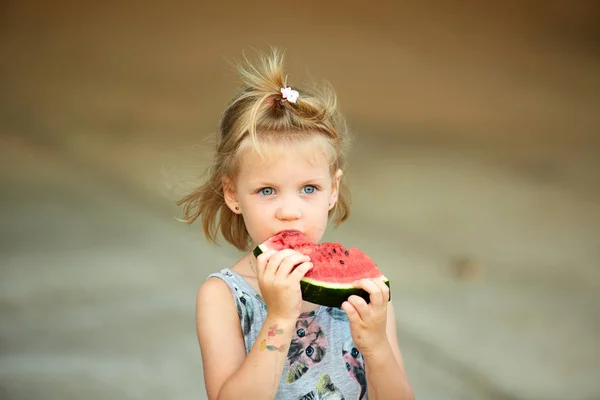 Adorable blonde girl eats a slice of watermelon outdoors. — Stock Photo, Image
