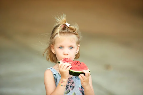 Adorable blonde girl eats a slice of watermelon outdoors. — Stock Photo, Image