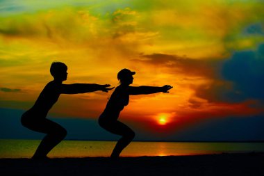 Eğitim ve plaj tarafından savaşçı poz gündoğumu veya günbatımı-dışında meditasyon yoga insanların.