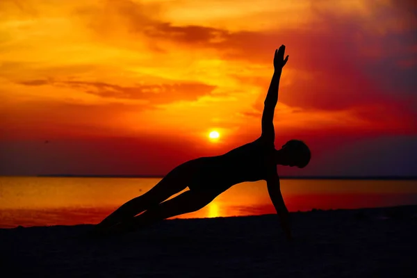 Σιλουέτα της γυναίκας που στέκεται στο yoga πόζα στην παραλία κατά τη διάρκεια ένα καταπληκτικό ηλιοβασίλεμα — Φωτογραφία Αρχείου