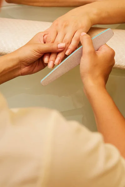 Closeup shot of a woman in a nail salon receiving a manicure by a beautician with nail file. Woman getting nail manicure. Beautician file nails to a customer — Stock Photo, Image