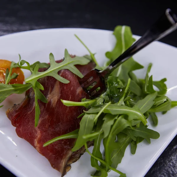 Slice of prosciutto or jamon with arugula leafs — Stock Photo, Image