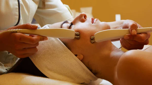 Cosmetologia. Mulher bonita na clínica do spa que recebe estimulando o tratamento facial elétrico do terapeuta. Closeup de rosto feminino jovem durante a terapia de microcorrente. Tratamento da beleza . — Fotografia de Stock