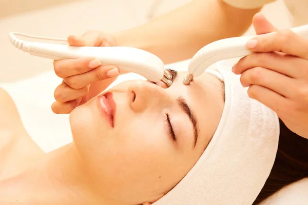 Cosmetologia. Mulher bonita na clínica do spa que recebe estimulando o tratamento facial elétrico do terapeuta. Closeup de rosto feminino jovem durante a terapia de microcorrente. Tratamento da beleza . — Fotografia de Stock