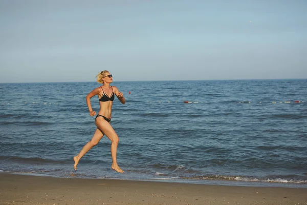 Πλάγια όψη του μια γυναίκα που τρέχει στην παραλία με την ορίζοντα και την θάλασσα στο παρασκήνιο — Φωτογραφία Αρχείου