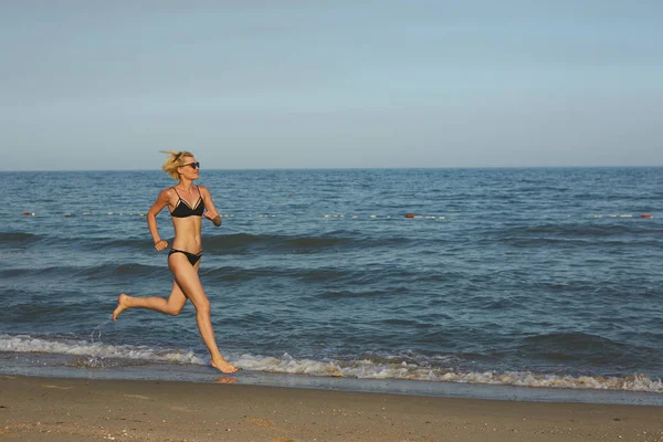 Vista laterale di una donna che corre sulla spiaggia con l'orizzonte e il mare sullo sfondo — Foto Stock