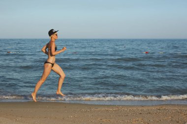 Etkin sportif kadın okyanus sörf zinde ve Sağlık tutmak için su havuzu tarafından çalıştırın. Günbatımı siyah kum plaj güneş ile arka plan. Kadın fitness, egzersiz ve spor etkinliği yaz aile tatil koşu.