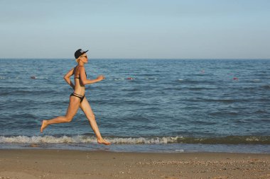 Etkin sportif kadın okyanus sörf zinde ve Sağlık tutmak için su havuzu tarafından çalıştırın. Günbatımı siyah kum plaj güneş ile arka plan. Kadın fitness, egzersiz ve spor etkinliği yaz aile tatil koşu.