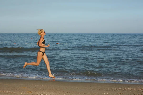 Vista lateral de uma mulher correndo na praia com o horizonte e o mar ao fundo — Fotografia de Stock