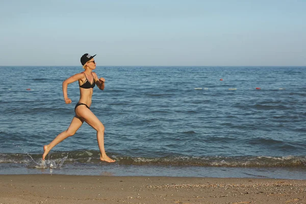 Mulher bonita sexy e feliz em biquíni correndo na praia. Num boné com a inscrição Rainha. Efeito filme . — Fotografia de Stock