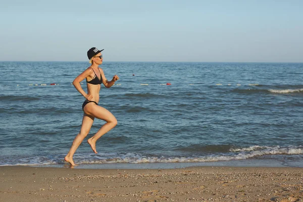 Sexy und glücklich schöne Frau im Bikini am Strand laufen. in einer Mütze mit der Aufschrift Queen. Filmeffekt. — Stockfoto