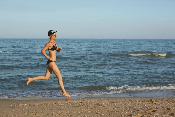 Aktív sportos nő szaladni ocean surf víz medence tartani fit és egészség. Naplemente fekete homokos strand háttér nap. Női fitness, jogging edzést és sport tevékenység a családi nyaralás. — Stock Fotó