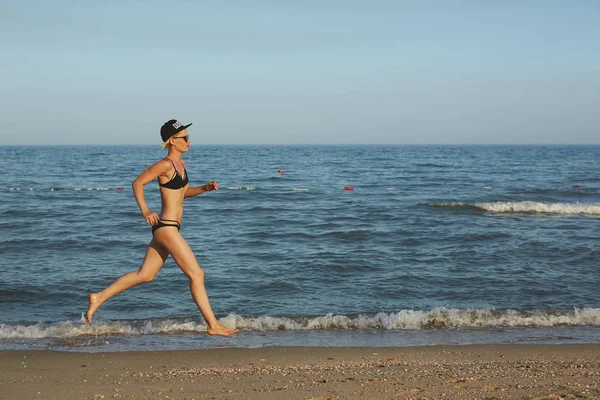 Mulher bonita sexy e feliz em biquíni correndo na praia. Num boné com a inscrição Rainha. Efeito filme . — Fotografia de Stock