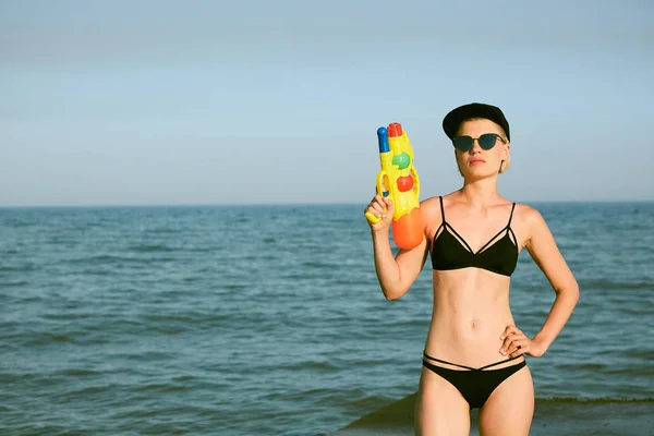 Giovane donna felice con un cappello con la parola regina che gioca con pistola ad acqua. Effetto pellicola — Foto Stock