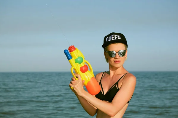 Giovane donna felice con un cappello con la parola regina che gioca con pistola ad acqua. Effetto pellicola — Foto Stock