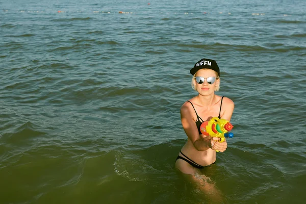 Šťastná mladá žena v čepici s královnou slovo hrát s vodní pistole. Efekt filmu — Stock fotografie