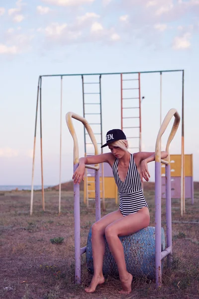 Beautiful woman in black and white striped swimsuit on the old sports ground. Film effect. — Stock Photo, Image