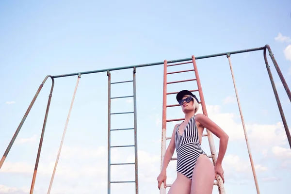 Beautiful woman in black and white striped swimsuit on the old sports ground. Film effect. — Stock Photo, Image