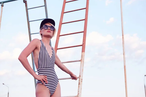 Beautiful woman in black and white striped swimsuit on the old sports ground. Film effect. — Stock Photo, Image