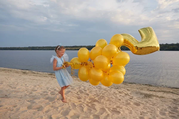 Menina com muitos balões dourados na praia ao pôr do sol — Fotografia de Stock