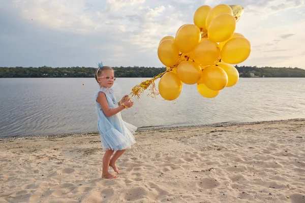 Gün batımında sahilde birçok altın balon ile küçük kız — Stok fotoğraf